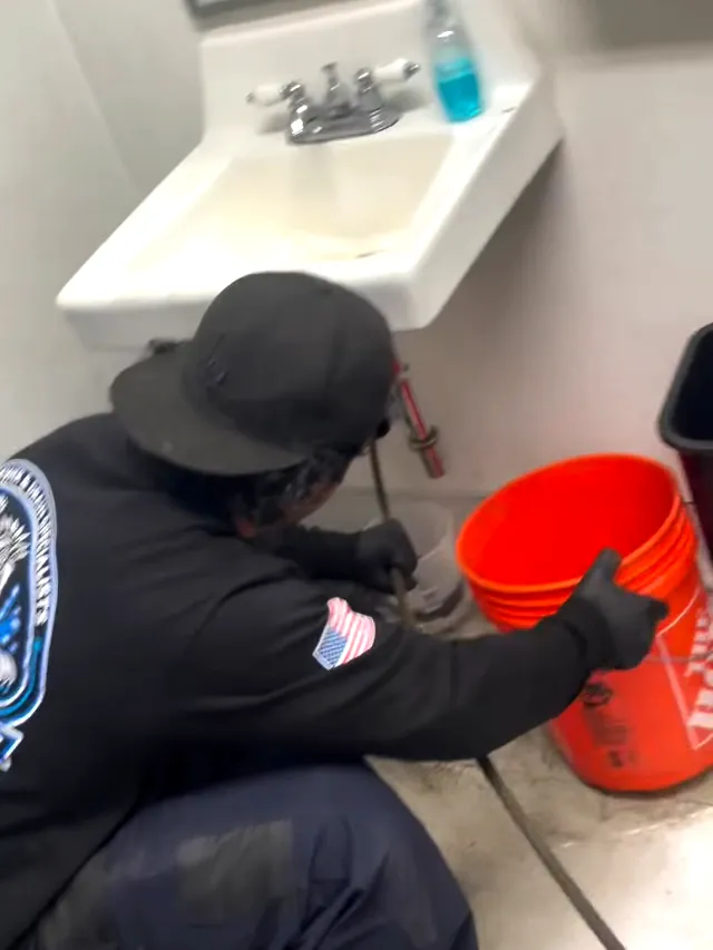 A technician feeding a drain cable into a lavatory waste line with a bucket set under the trap