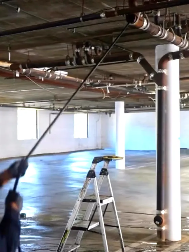 A technician running a hydro jetting hose up into the overhead waste lines of a parking structure