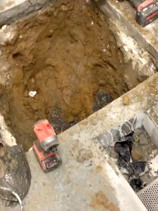 An opened trench in a concrete floor with the failed drain line exposed and tools laid around it